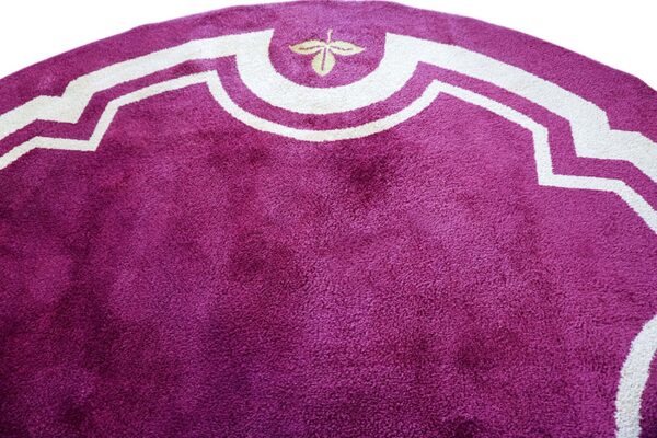 Close-up of a deep purple shag rug with a white, stylized geometric border and small leaf.