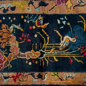 Close-up of a high-pile rug featuring a navy blue field and brown border with detailed multi-colored floral motifs.