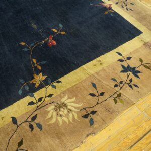 Dark navy and tan rug with colorful scrolling floral patterns and a yellow stripe border on wood flooring.
