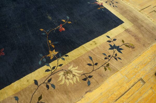 Dark navy and tan rug with colorful scrolling floral patterns and a yellow stripe border on wood flooring.
