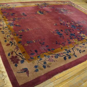 Berry-colored area rug with ornate blue and yellow floral vines bordered by tan and maroon on distressed wood floors.