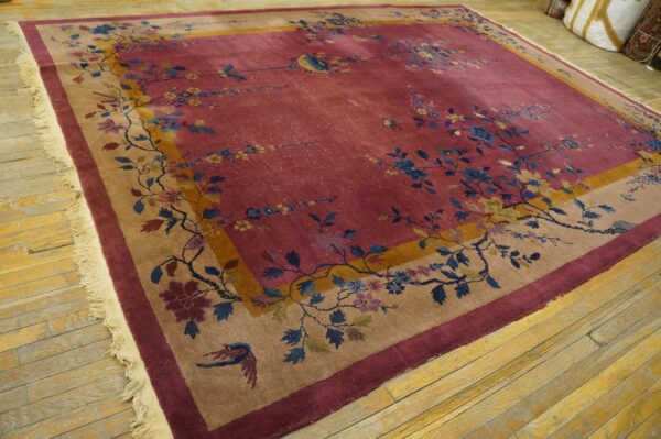 Berry-colored area rug with ornate blue and yellow floral vines bordered by tan and maroon on distressed wood floors.