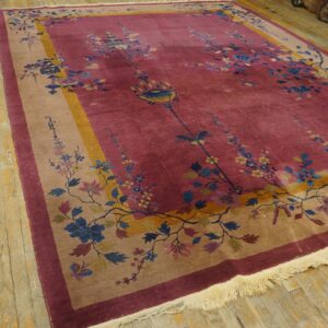 Magenta and tan floral rug displayed on rustic light wood planks, showing detailed fringe.