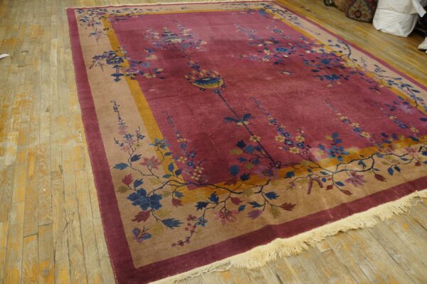 Magenta and tan floral rug displayed on rustic light wood planks, showing detailed fringe.
