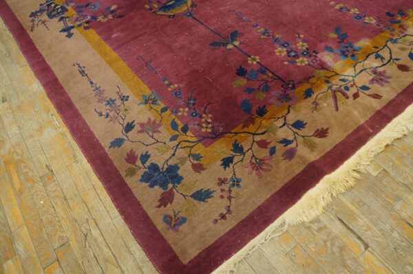 Magenta rug with blue and yellow florals and tan border rests on distressed wood plank flooring.
