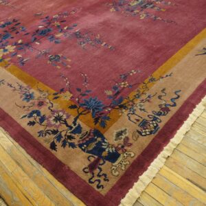 Rose and beige rug featuring ornate blue and gold floral patterns on worn wood flooring.