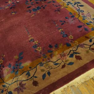 Dusty rose rug with blue and yellow floral vines, framed by a tan and gold bordered field on wood flooring.