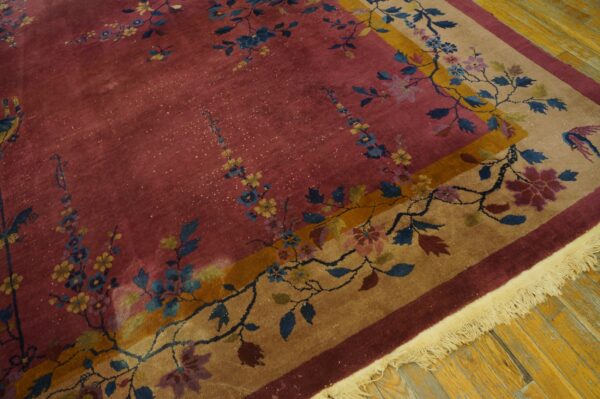 Dusty rose rug with blue and yellow floral vines, framed by a tan and gold bordered field on wood flooring.