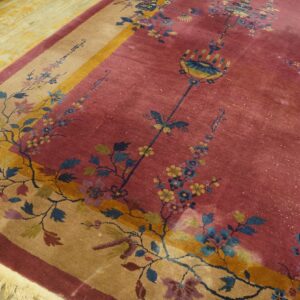 A dusty rose rug features a tan and yellow floral border, resting on worn yellow hardwood floors.