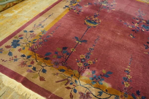 A dusty rose rug features a tan and yellow floral border, resting on worn yellow hardwood floors.