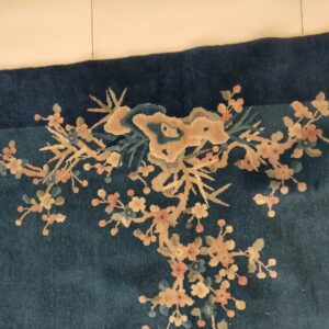 High-pile, dark blue rug showing a gold and pink floral branch pattern near a tiled edge.