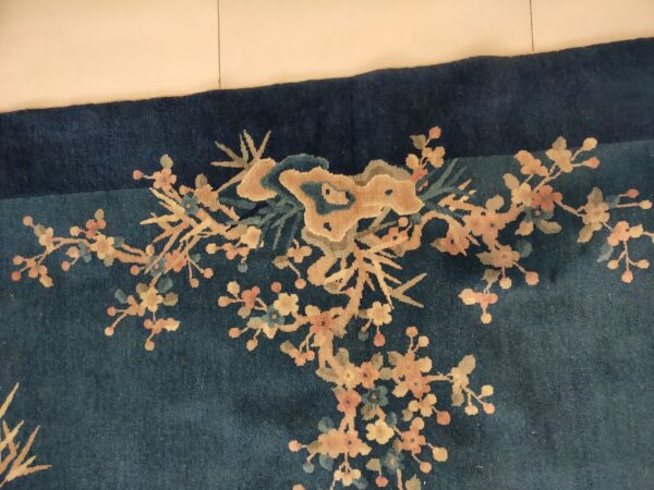 High-pile, dark blue rug showing a gold and pink floral branch pattern near a tiled edge.