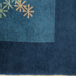 Dark blue rug corner showing peach and pale green starburst motifs and a woven beige fringe.