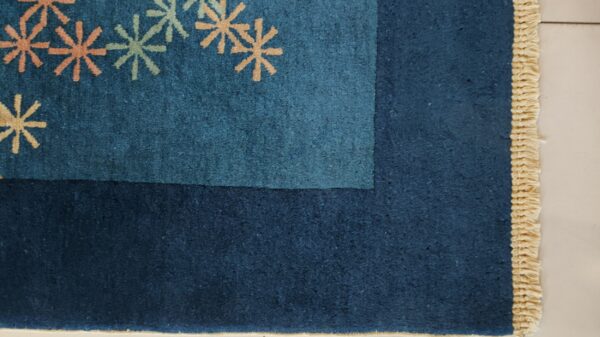 Dark blue rug corner showing peach and pale green starburst motifs and a woven beige fringe.
