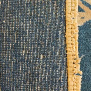 Reverse side of a blue rug revealing a speckled weave, beige looped edge, and patterned blue pile.