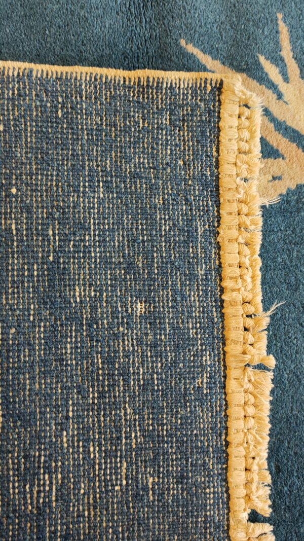 Reverse side of a blue rug revealing a speckled weave, beige looped edge, and patterned blue pile.