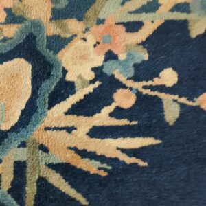 Detail of a plush rug showing large gold, blue-green, and coral florals on a dark navy blue background.