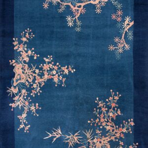 A deep indigo rug bordered by dark navy features scattered pink and peach flowering branches.