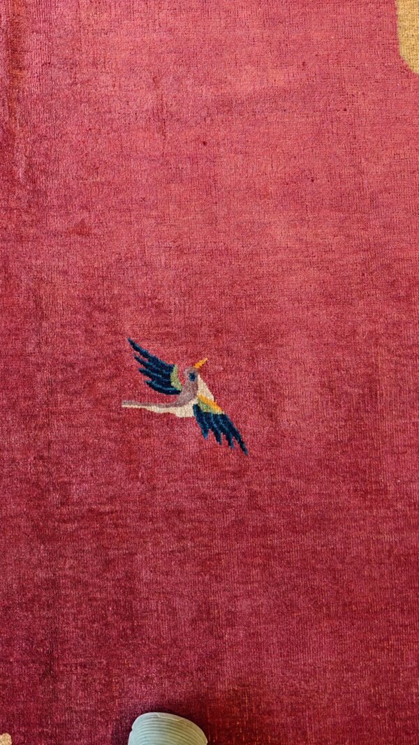 Close-up of a deep magenta rug featuring a small, stylized multicolored flying bird design.