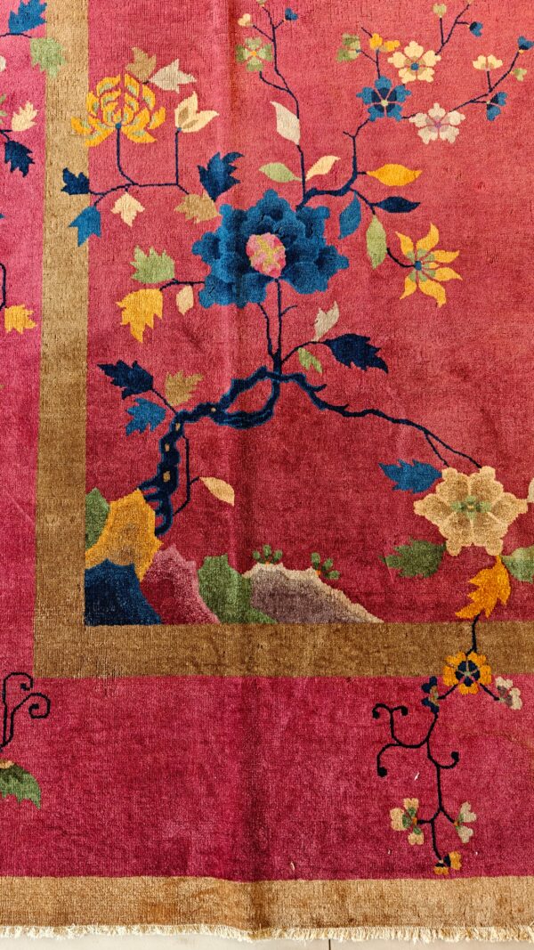 Magenta rug corner featuring gold border and vibrant blue, yellow, and green floral branch motifs.