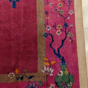 Magenta rug with a stylized green vase, flowering branches, and a decorative lantern pattern within a tan border.