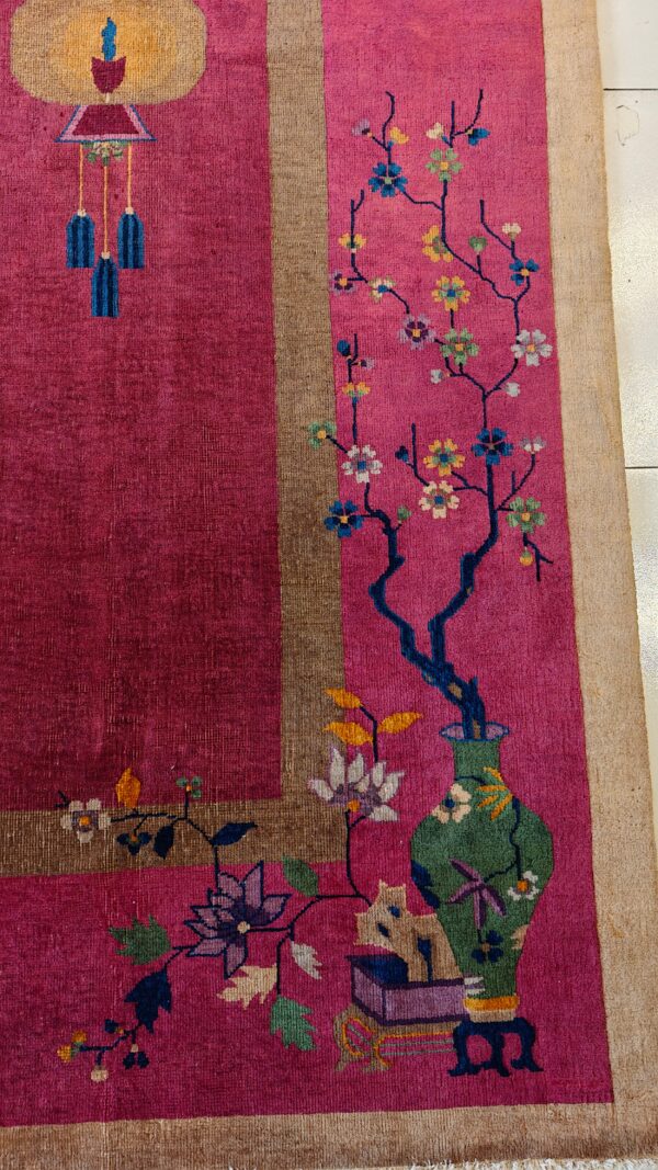 Magenta rug with a stylized green vase, flowering branches, and a decorative lantern pattern within a tan border.