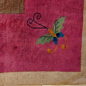 High-pile magenta rug with a green and blue butterfly pattern, lying on light distressed wood flooring.