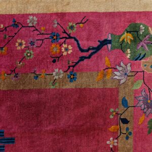 Deep pink rug detail shows a stylized green vase, multicolored blossoms, and a wide tan border.