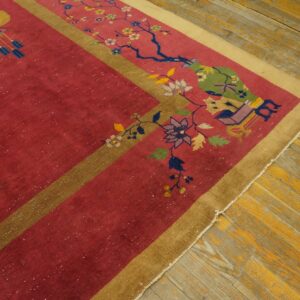 Red and gold rug with detailed floral and lantern pattern lies on worn yellow wood flooring.