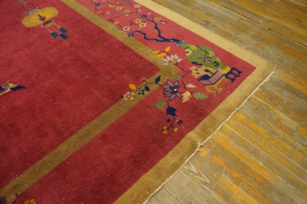 Red and gold rug with detailed floral and lantern pattern lies on worn yellow wood flooring.