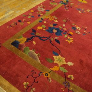 Red rug with multicolored floral and bird patterns, gold and brown borders, resting on light wood flooring.