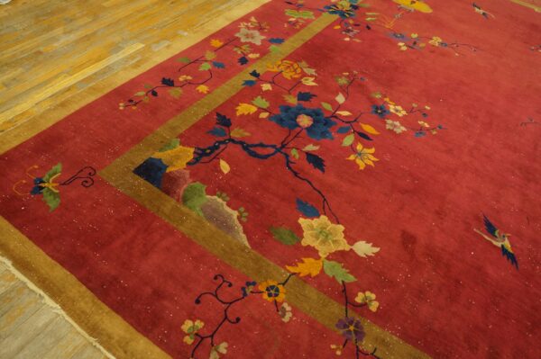 Red rug with multicolored floral and bird patterns, gold and brown borders, resting on light wood flooring.