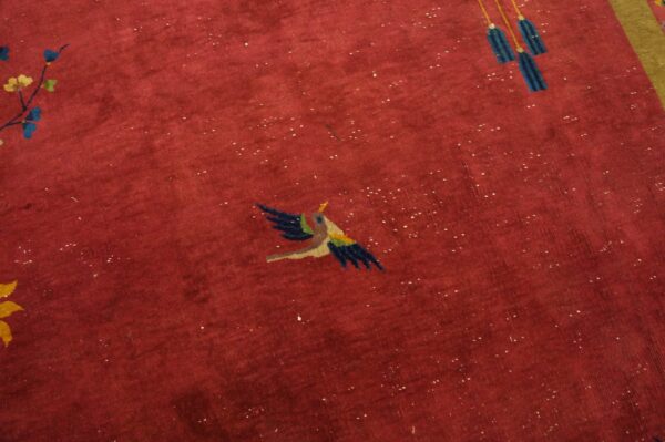 Detail of a red medium-pile rug showing a stylized flying bird and blue hanging tassels.