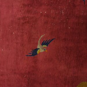 High-pile maroon rug detail showing a multicolored bird, florals, and gold lantern element.