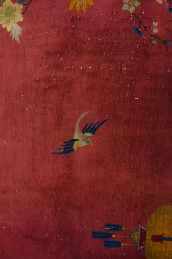High-pile maroon rug detail showing a multicolored bird, florals, and gold lantern element.
