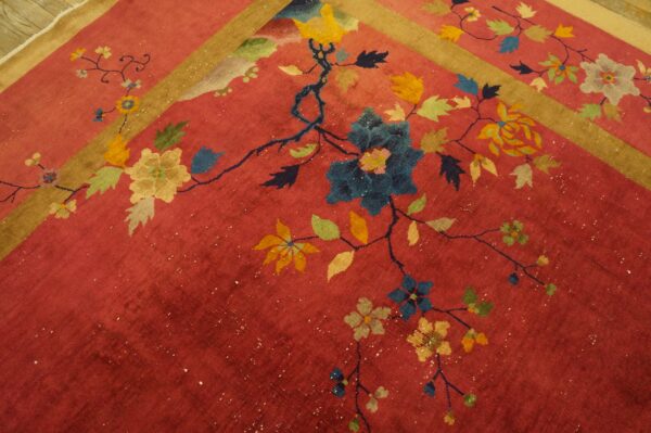 Red rug detail showing colorful blue, yellow, and green floral vines with a tan border stripe.