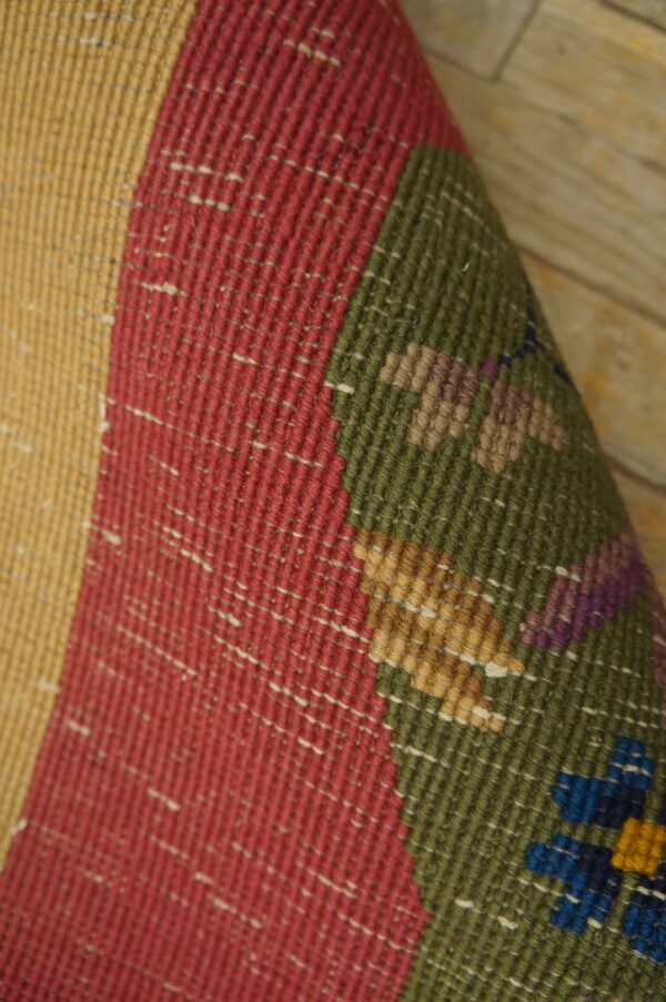 Detailed view of a flatweave rug featuring colorful bands and small geometric patterns on light wood flooring.