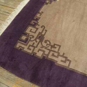 Beige low-pile rug with a dark purple border and geometric brown key pattern on distressed wood flooring.