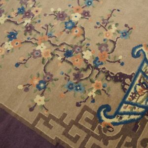 Tan rug featuring colorful floral vine motifs, large blue scrolls, and a brown Greek key style border.