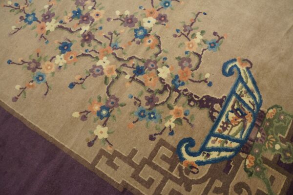 Tan rug featuring colorful floral vine motifs, large blue scrolls, and a brown greek key style border.