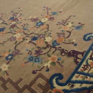 Muted tan rug with colorful blue, purple, and peach floral branches and a complex scrolled border.
