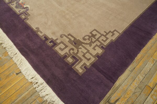 Low-pile rug in tan and purple featuring a detailed geometric border design on distressed light wood floors.
