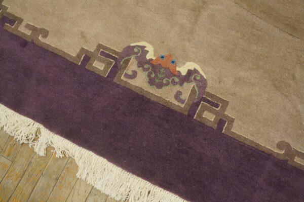 A rug featuring a beige field, purple border, multi-colored mythological motif, and fringe on wood floors.