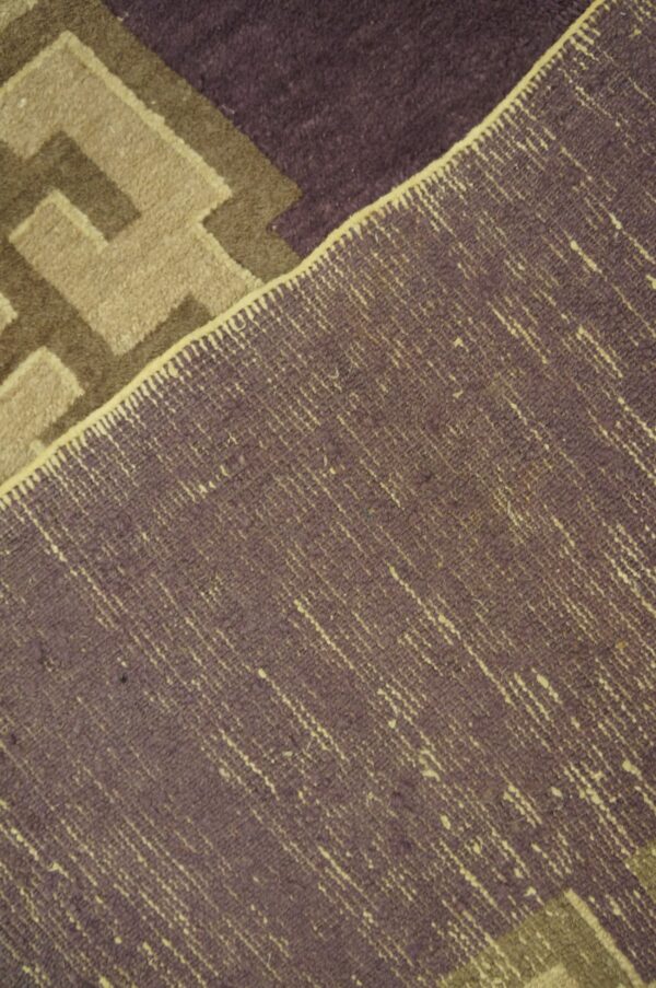 Textured close-up showing purple and beige geometric pile alongside the rug's coarse woven reverse.