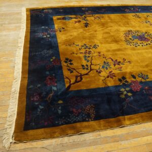 High-pile gold rug with a detailed navy blue botanical border on light, distressed wood flooring.