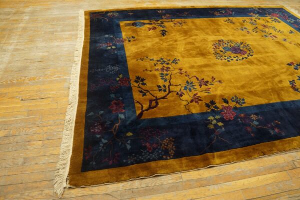 High-pile gold rug with a detailed navy blue botanical border on light, distressed wood flooring.