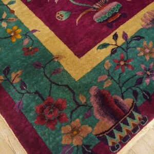 Close-up of a high-pile rug with teal field, magenta border, gold band, and multicolored flowers on wood floor.