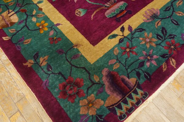 Close-up of a high-pile rug with teal field, magenta border, gold band, and multicolored flowers on wood floor.