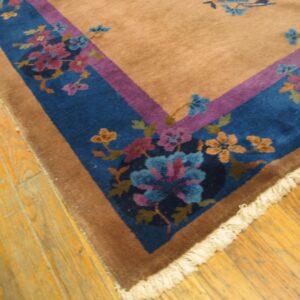 Tan area rug with a blue and purple floral border corner on rustic wooden planks.