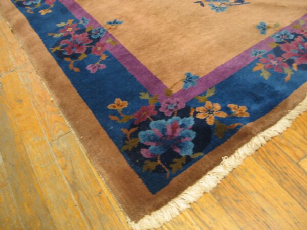 Tan area rug with a blue and purple floral border corner on rustic wooden planks.